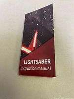Photo of the lightsaber instruction manual with cover showing a lit lightsaber and text 'LIGHTSABER Instruction manual'.