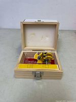 Open wooden box containing yellow tongue and groove router bits with foam padding in lid and clear plastic insert