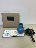 Rectangular ceramic plate with menorah and stars design, blue small ceramic vase, beige photo album with windowed cover, black cast iron egg fryer with seven molds