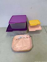 Five Tupperware plastic food storage containers with lids arranged in two stacks. Includes containers with purple, yellow and pink lids. One pink container sealed in original packaging.
