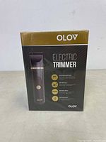 Front of the retail box showing OLOV Electric Trimmer in black with gold accents, key features listed including battery recharge time, 90-minute run time, and waterproof design.