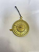 Top view of brass disk showing multiple engraved scales, numbers, and indicators used for nocturnal and tidal calculations. The disk has a black cord attached.