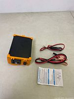 Power inverter device with cables and instruction manual on a beige surface.