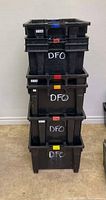 Stack of four black plastic industrial bins labeled 'DFO' with various colored clips.