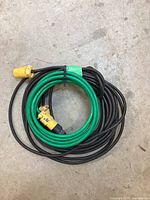 Both green 10 foot and black 50 foot extension cords coiled together with yellow plug and socket covers on a concrete floor.