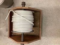 Spool of white 14-2 Romex house wire mounted on wooden holder, showing coiled wire and metal spindle.