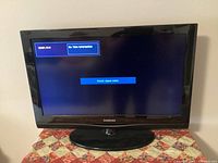 Front view of the 32-inch Samsung TV powered on showing input message 'Check signal cable.' The TV is mounted on a black oval base stand.