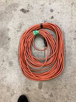 36-foot orange extension cord coiled on concrete floor, showing plug end.