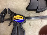 Close-up of a yellow/black Quick-Grip clamp showing label and trigger handle.