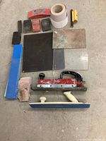 Top down view showing all items including sanding blocks, sandpaper rolls, and the air sander tool, arranged on concrete floor.