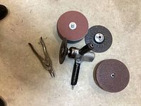 Air dual-action orbital sander with several stacks of round sanding discs and snips on concrete floor.