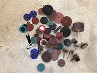 Top view showing assorted abrasive discs, flap wheels, sanding sleeves, and a wire brush attachment arranged on a surface.