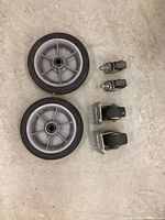 Two grey plastic spoked wheels with black rubber tires, two smaller metal swivel castors with rubber wheels and two larger swivel castors with mounting plates.