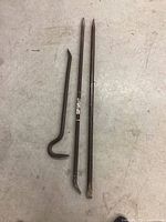 Photo showing three rusted metal bars on concrete floor: a small crow bar and two longer bars, one pry bar and one digging bar.