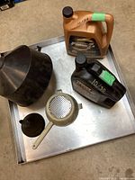 View of two oil containers, two funnels, and aluminum drip tray arranged on tray.