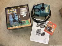 Sharpener laid on floor with power cord coiled, box next to it showing branding and model number, instruction manual and accessories.