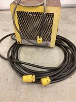 Closer view of heater front grille with attached power cord coiled on floor, highlighting paint overspray and wear.