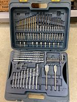 Open case showing organized layout of various drill bits and accessories including metal, wood, and concrete bits.