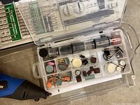 Close-up photo of a carrying case with numerous rotary tool attachments including grinding stones, sanding drums, polishing pads, and bits.