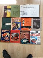 Photo of 12 automotive-related books and manuals spread on a floor showing covers and titles for restoration, wiring, maintenance and parts for Ford vehicles and general automotive topics.