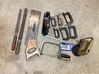 Photo showing metal files/rasps, wooden-handled handsaw, metal hand plane, coping saw, multiple sizes of C clamps, electric jigsaw, and new blades pack.