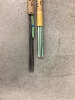 Two paper tubes containing rods: one with thin dark welding rods and one with light green brazing rods. Tubes have handwritten labels describing rod size and type.