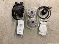 Top down photo showing respirator mask, two filters, plastic container, hose attachment, and replacement filters.
