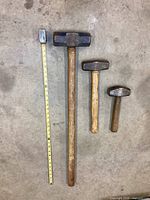 Overhead photo of four sledgehammers with measuring tape laid beside them showing size variation.