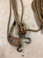 Closeup of two wooden pulley blocks attached to natural fiber rope showing metal hooks and rope thickness.