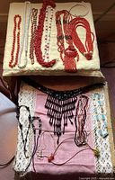 Photo of 14 vintage necklaces laid out on a cushion and fabric, featuring red, white, and black beads of various styles and lengths.