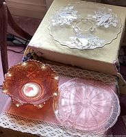 Three glass items displayed together: silver resist bird platter elevated on legs, carnival glass bowl with ruffled edges, pink Depression glass platter with geometric patterns.