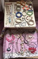 Overview photo showing assorted bracelets and necklaces on table, displaying varied colors and materials including metal bangles, plastic beads, and rhinestone details.