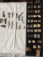 Photo showing 20 cufflinks and 16 tie clips arranged on a white cloth and black display strip