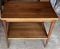 Full front view of teak two tier side table showing both shelves and tapered round legs.