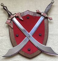 Front view of the shield-shaped wooden plaque with two crossed scimitars with detailed embossed colored brass handles on red felt background.