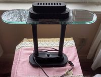 Black metal desk lamp with clear glass reflector on top, dual vertical supports, black base and dimmer switch, shown unlit on table.