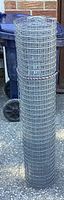 A standing roll of silver galvanized chicken wire mesh on a concrete surface.