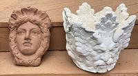 Front view of the pottery clay goddess face wall plaque and the white concrete planter with faces.