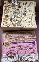 Full overview of brooches and necklaces laid out on beige and pink fabric, showing variety of styles, colors, and materials
