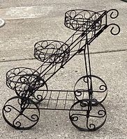 Side angle showing the stair-stepped, 3-tier design with black metal pot holders and large scroll decorative wheels.