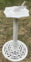 Full view of solid iron sundial standing on decorative iron pedestal base in garden setting.