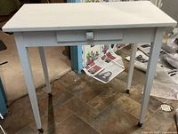 Front view of the white wooden side table showing tabletop, front drawer, and legs.
