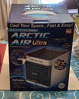 Box front showing Arctic Air Ultra branding and features such as 3 speed control, LED night light, quick and easy top-fill water tank, and 2x cooling power.