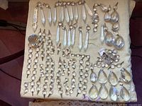 Full view of the assortment of facetted glass crystals on a cloth surface showing various large and small crystals, strings, and single pieces.