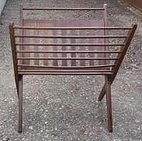 Front view of vintage fold out teak magazine rack showing slatted panel and folding legs.