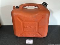 Front view of the orange gas can showing textured surface, carry handle, black cap, and warning labels on the body.