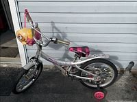 Full side view of silver Avigo Purple Rain bike with training wheels and yellow cartoon face attachment on handlebars.