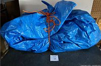 Photo showing the folded large blue polyethylene tarp with orange rope drawstring securing it.