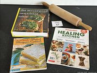 Lot includes three cookbooks and one wooden rolling pin displayed on a black surface.