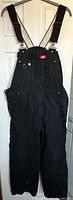 Full front view of Dickies black cotton overalls with adjustable shoulder straps, multiple pockets, and a red logo patch on the bib.